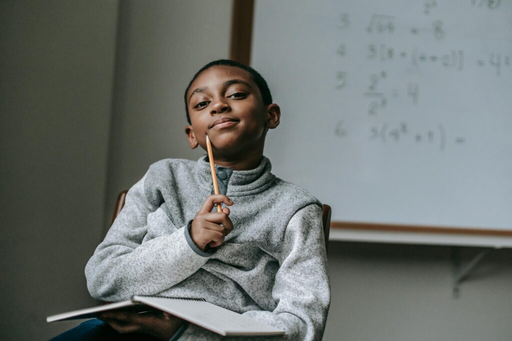 Young African American boy pensively studying in a classroom with math equations on a whiteboard.