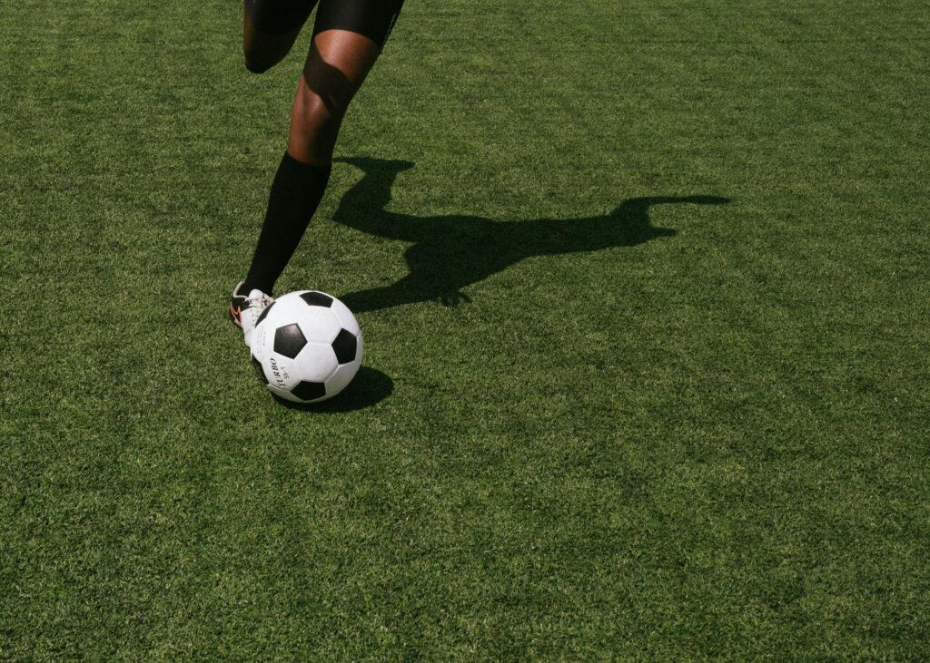 Cropped shot of a soccer player in motion, performing a kick on a grassy sports field under daylight.